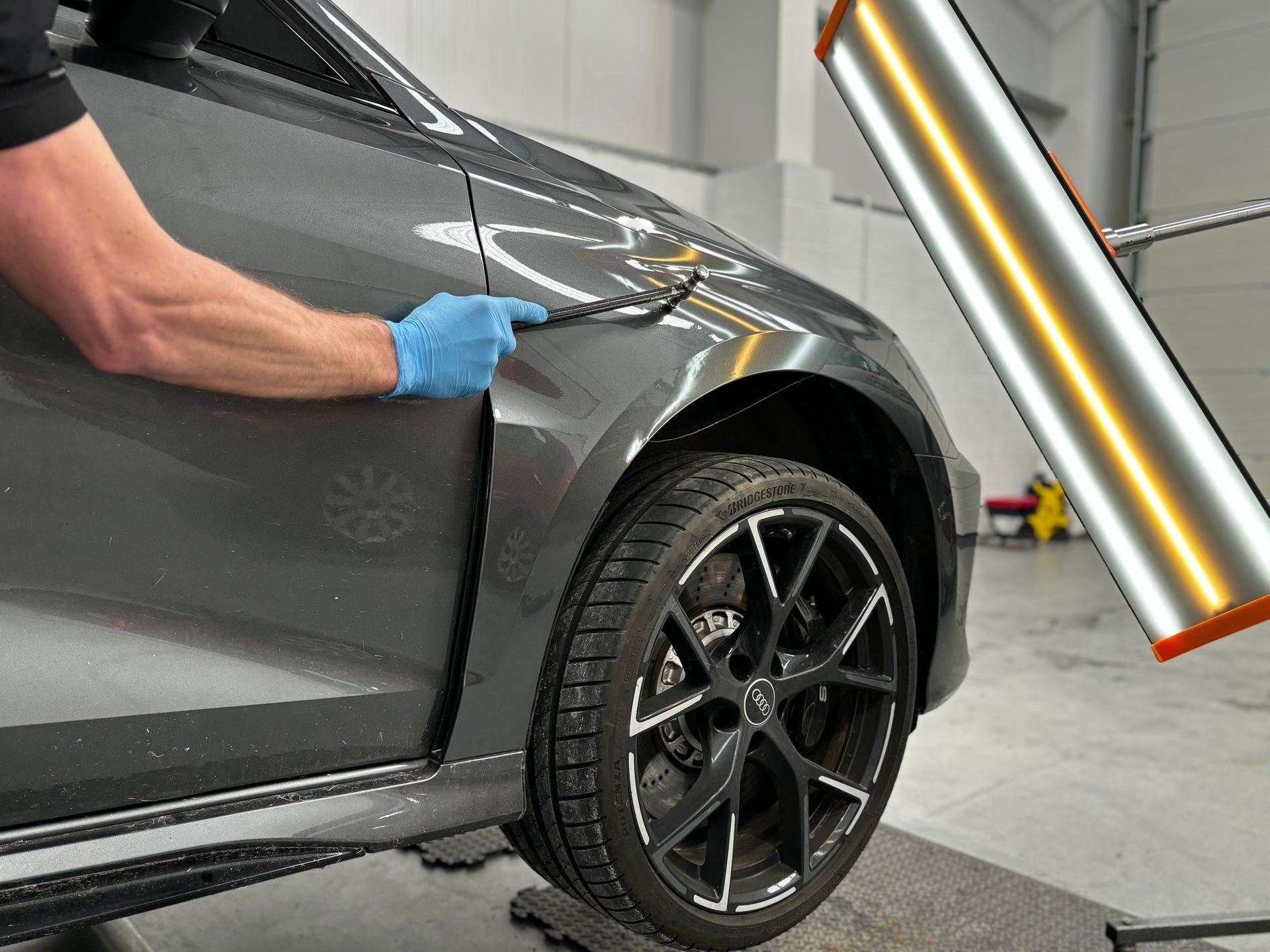 Technician inspecting a car's front fender with a dent removal light in an automotive workshop.